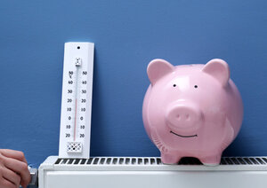 Sparschwein und Thermometer auf einer modernen Heizung, die das Einsparpotenzial durch staatliche Förderungen und effizientes Heizen verdeutlichen.